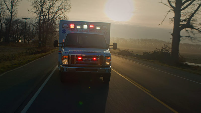image from video of a Medix ambulance with lights on driving down a county highway at sunset